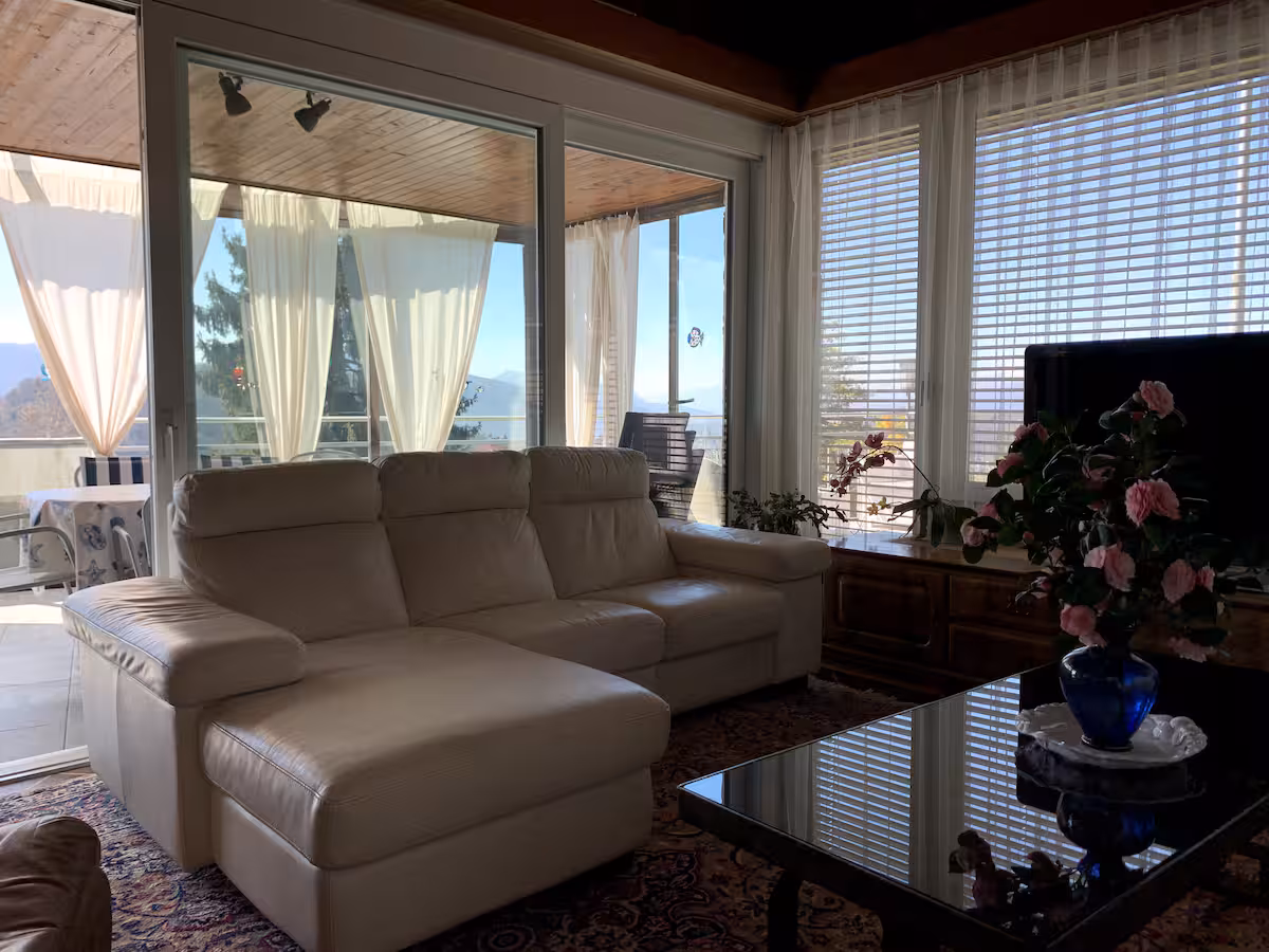 Salon avec canapé d'angle beige et baies vitrées donnant sur le jardin