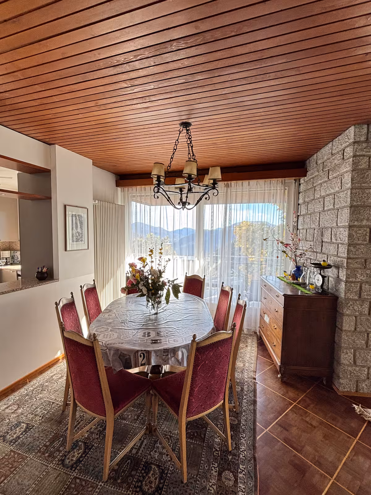 Salle à manger avec mur en pierres apparentes, chaises bordeaux et grande baie vitrée