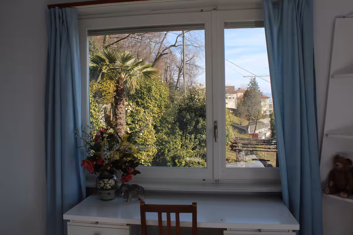 Fenêtre de chambre avec rideaux bleus, vue sur le jardin et les collines