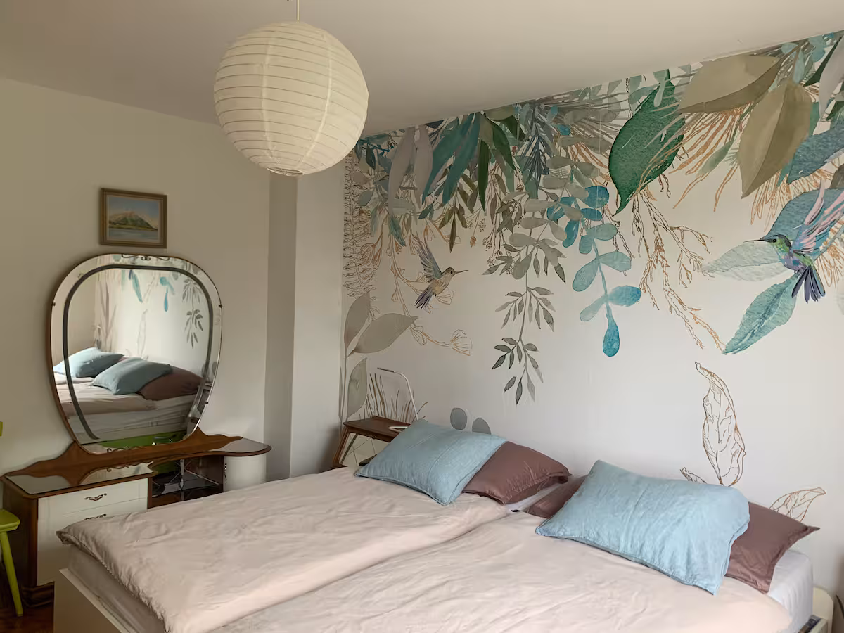 Chambre avec papier peint à motifs végétaux, lit et miroir ovale