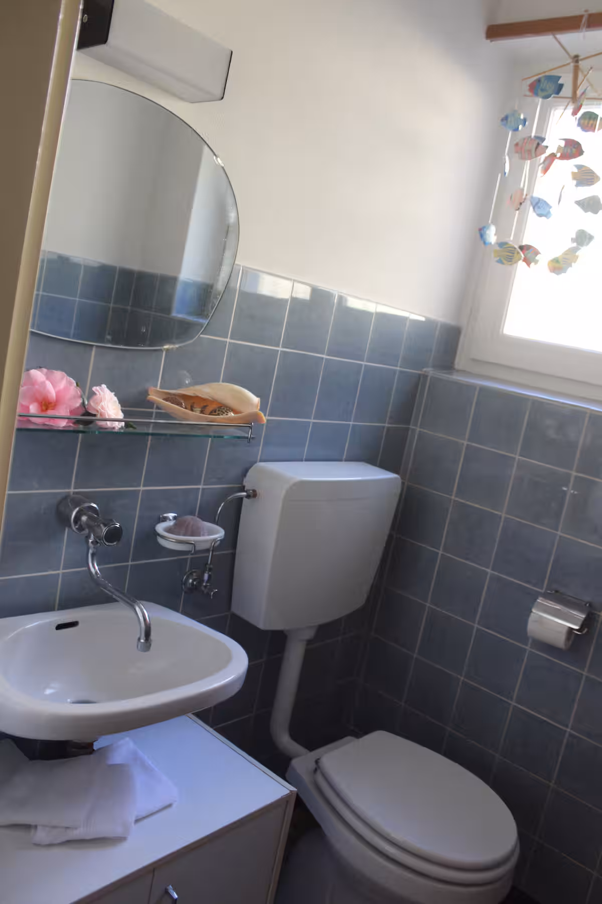 Salle de bain avec lavabo, miroir ovale et mobile de poissons