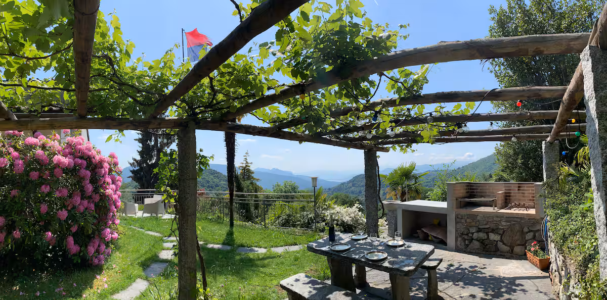 Table en pierre sous la pergola de vigne avec verres et bouteilles, coin barbecue en pierre