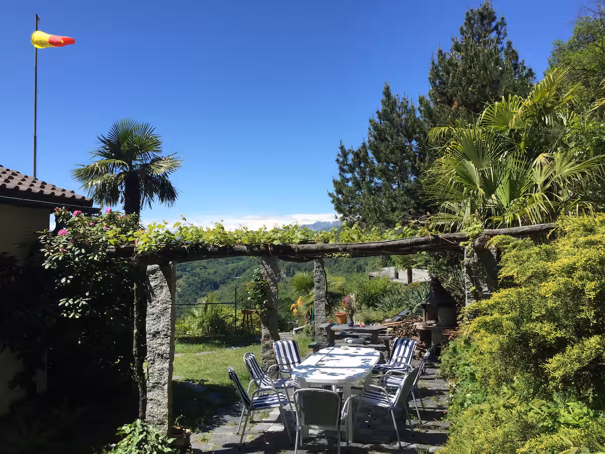 Pergola du jardin avec table, chaises et palmiers, vue sur les collines