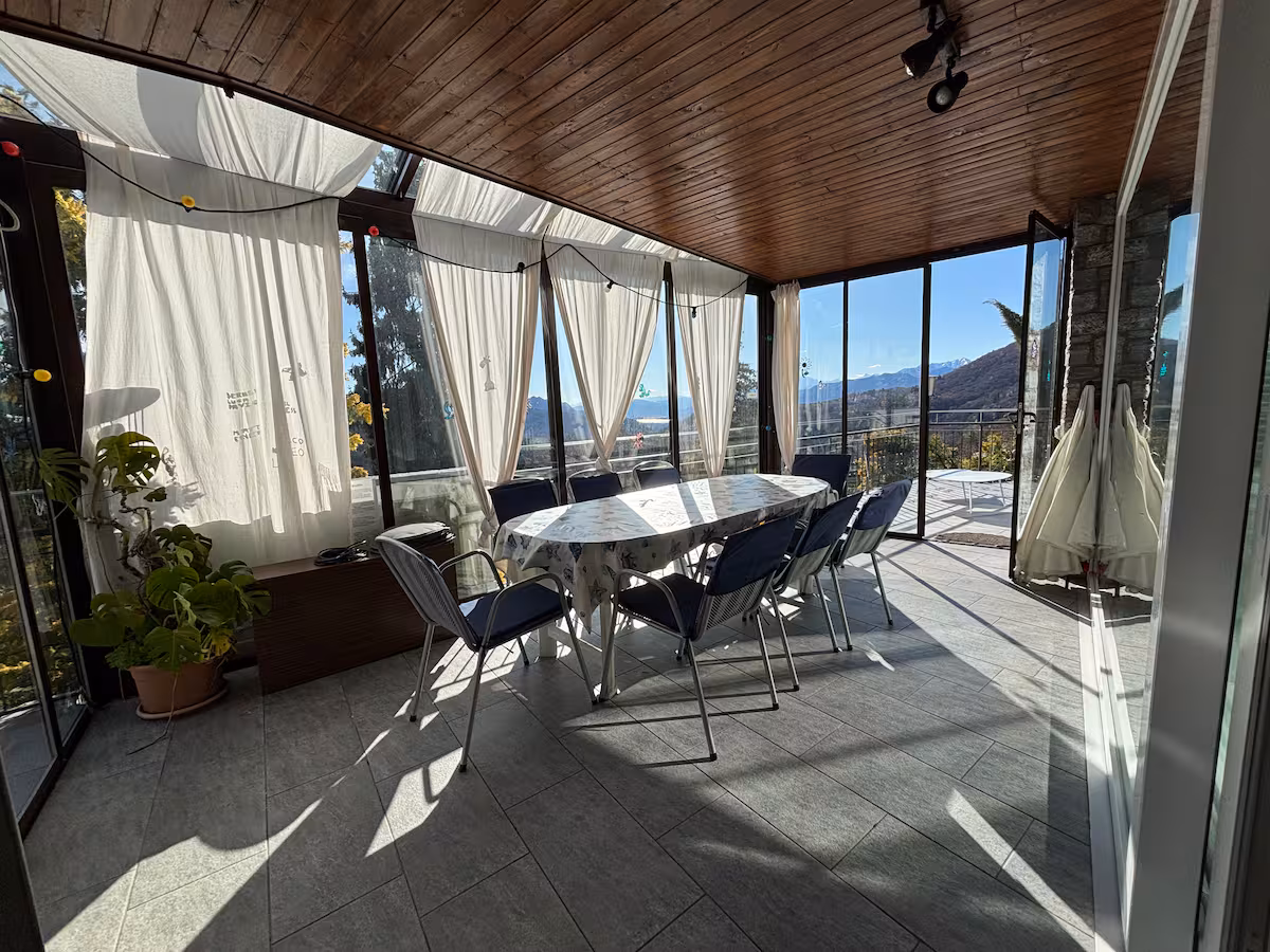 Terrasse en bois avec grande table et rideaux, vue sur les collines
